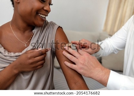 A beautiful smiling brave African woman sits with her pediatrician at the office as she receives a bandage after a vaccination. Medical healthcare worker puts plaster on the girl arm after vaccination