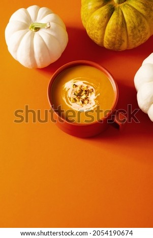 Autumn pumpkins soup with vegetables on orange background, modern concept, copy space, vertical
