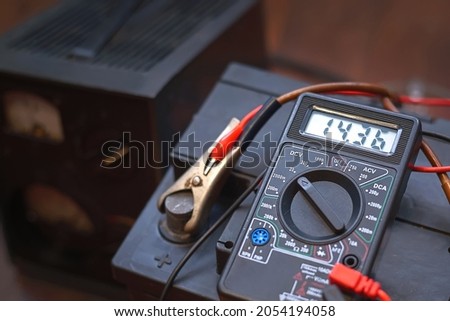 Checking voltage with multimeter and charging car battery with charger from home electricity. Recovery of acid batteries, resuscitate car battery. Voltmeter to check voltage level on car battery Royalty-Free Stock Photo #2054194058