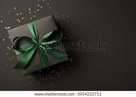 Top view photo of stylish giftbox with green ribbon bow and golden confetti on isolated black background with empty space Royalty-Free Stock Photo #2054222711