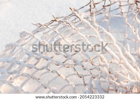 Abstract winter photo with rusty fence cage Rabitz covering with white snow on a sunny day. Broken fence in an abandoned Russian village