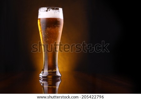 Tall glass of light beer on a dark background lit yellow Royalty-Free Stock Photo #205422796