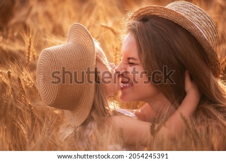 Close-up portrait of mother and daughter in straw hats in a slice of wheat field. A little girl kisses, hugs a young woman in spikelets of rye. Natural agricultural texture. Girls have fun, laugh