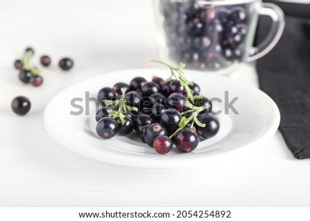Plate with ripe black currant on light wooden background
