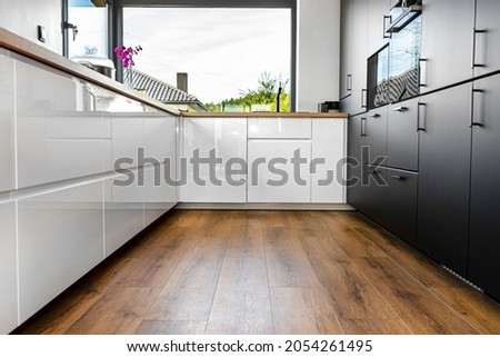 A modern kitchen with white and black fronts and a large corner window, vinyl panels on the floor. Royalty-Free Stock Photo #2054261495