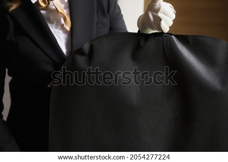 Black garment, suit travel bag. the hands of a hotel worker in white gloves. Royalty-Free Stock Photo #2054277224