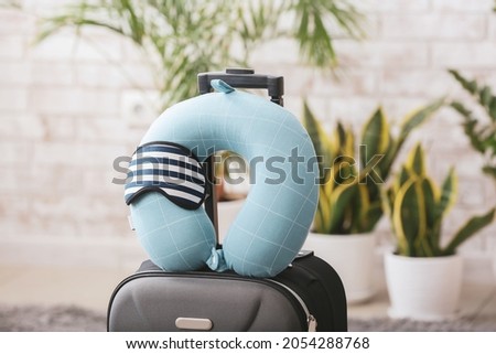 Travel pillow, sleep mask and suitcase on floor in room Royalty-Free Stock Photo #2054288768