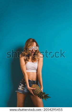 Woman portrait holding pineapple against colorful blue background with copy space. 