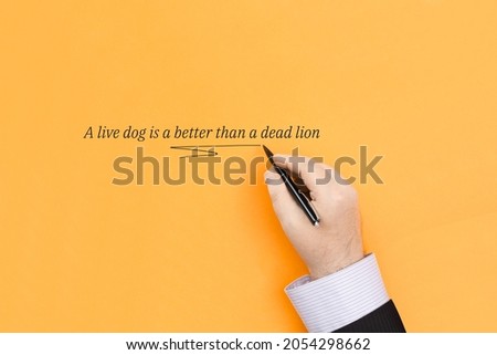 The proverb A live dog is a better than a dead lion means It is better to be a living coward than a dead hero. The inscription on an orange background.