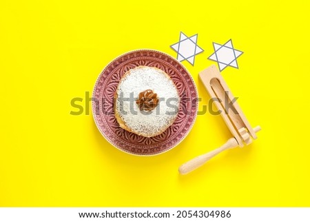 Tasty donut for Hanukkah and rattle on color background