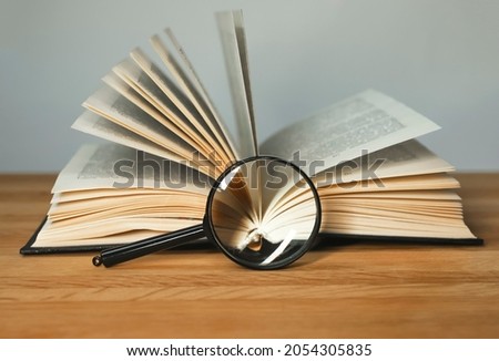 Magnifying glass and open books with turning pages on wood table. Reading and studying concept. Royalty-Free Stock Photo #2054305835