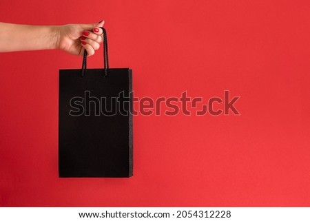 the concept of black friday. black bag in hand on a red background with space for text. High quality photo with copy space
