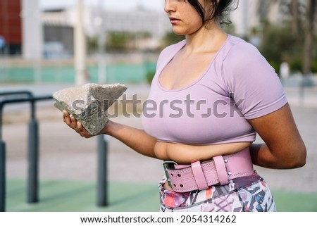 Strong Hispanic sportswoman lifting concrete block during outdoor functional workout