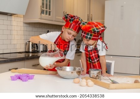 children in chef costumes prepare dough from flour, milk, eggs and butter for Christmas pastries. brother and sister are cooking festive dinner, cookies for new year in the kitchen. High quality photo