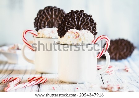 Two cups of hot cocoa with whipped cream, crushed candy canes and Pizzelle cookie wafers for Christmas. Extreme selective focus with blurred foreground and background. 