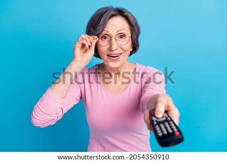 Photo of happy excited cheerful good mood mature woman in glasses watching television isolated on blue color background