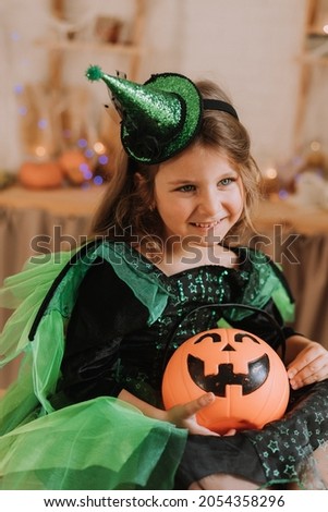 charming little girl in a green Halloween costume of a witch or sorceress with a pumpkin lantern jack, a basket for sweets in her hands. autumn concept. High quality photo