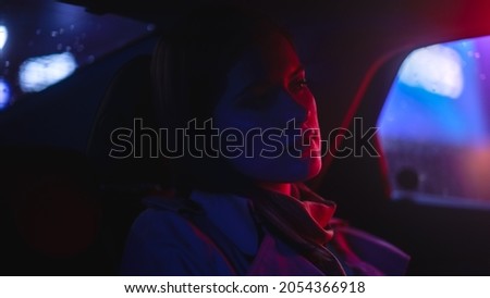 Close Up Portrait of a Female Commuting Home in a Backseat of a Taxi at Night. Beautiful Woman Passenger Looking Out of Window while in a Car in City Street with Working Neon Signs.