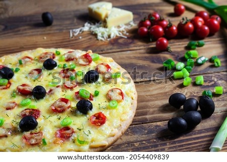 homemade pizza and pizza ingredients: olives, onions, cheese, tomatoes and a pizza knife on a wooden table
