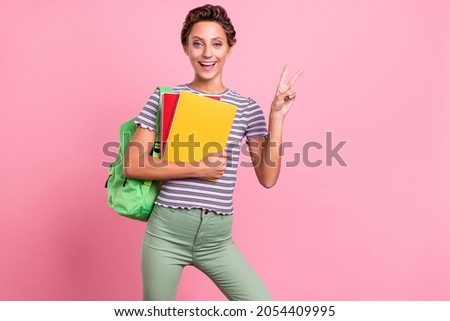 Photo of optimistic young school lady hold books show v-sign wear bag white t-shirt jeans isolated on pink color background