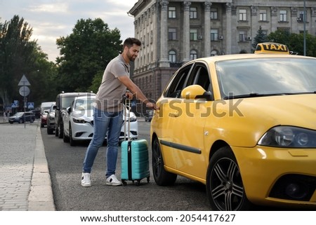 Handsome young man with suitcase getting in taxi on city street Royalty-Free Stock Photo #2054417627
