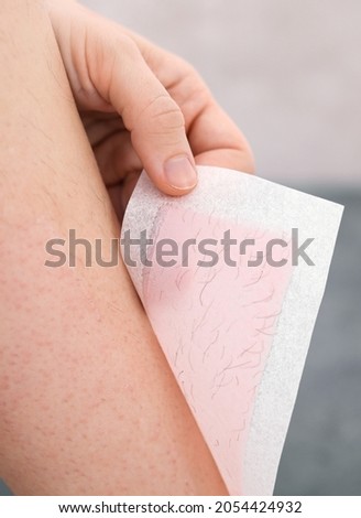 Hairy legs. Woman using beeswax stripe to shave her leg. Depilation procedure with wax, close up. Hair removal concept.