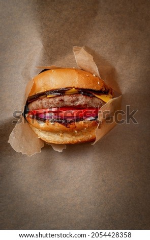 A hand holds a burger against a backdrop of torn crane paper. A portion of beef and cheddar cheese. Special offer and cheap price on fast food.
