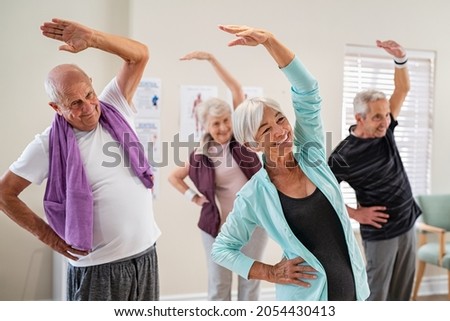 Group of seniors doing stretching exercise together at retirement centre. Elderly men and old women exercising at nursing home during daily fitness. Retired couples exercising at care facility. Royalty-Free Stock Photo #2054430413