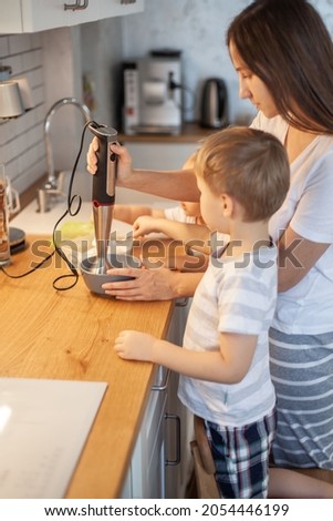 In the stylish home kitchen, mom, son and daughter prepare the icing for gingerbread. Preparation for Christmas concept. The girl helps her mother to beat with a blender.