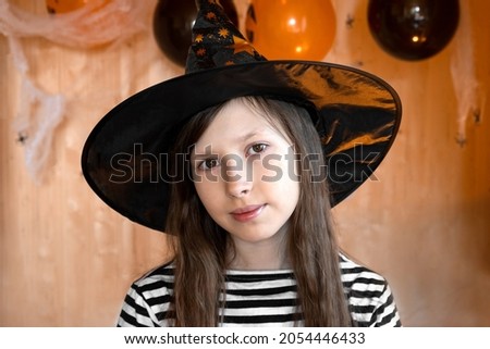 Portrait of adorable Teen Girl wearing Halloween hat, dancing and smiling. Halloween home family party concept. Happy caucasian little kid in a witch costume celebrating Halloween at home.