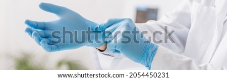 partial view of physician putting on blue latex gloves in clinic, banner Royalty-Free Stock Photo #2054450231