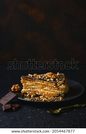 Biscuit cake with sour cream, nuts and chocolate glaze, on a black plate with chocolate on a dark textured background, Selective focus