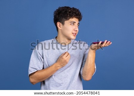 Record voice message. Portrait of young curly man, student using phone isolated over blue studio background with copyspace for ad. Concept of human emotions, healthy lifestyle, medicine, diversity