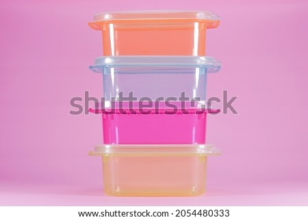 Small transparent plastic container for storing food. Four colorful transparent plastic containers stacked on isolated pink background. Food grade material. Royalty-Free Stock Photo #2054480333