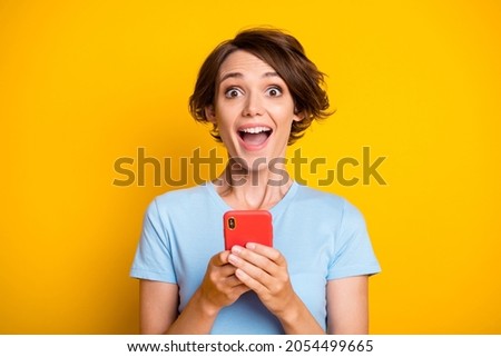 Photo of young excited girl happy positive smile amazed surprised use cellphone chat isolated over yellow color background