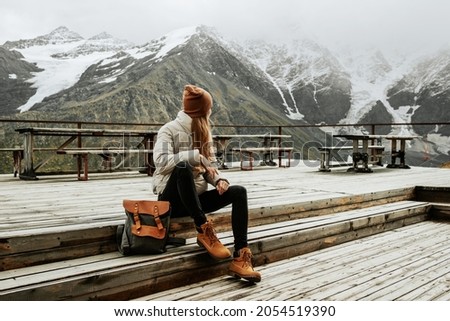 Girl traveler with backpack enjoy mountain nature sitting on wooden bridge. Cheget, Kabardino-Balkaria, Russia. Royalty-Free Stock Photo #2054519390