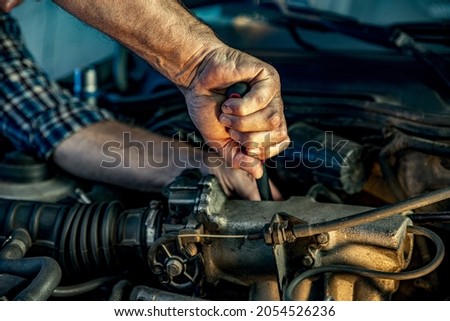 Repairman's male hands with a wrench. Vehicle fitter inspecting used car engine. Car components, belts, hoses, labor arm close up in the open hood of the car. Service center, auto repair shop Royalty-Free Stock Photo #2054526236