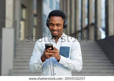 young african student listening to music from smartphone using big headphones, smiling from the convenience of using the app