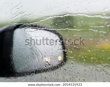 Car window and side mirror in splashes of rain and glare from other cars