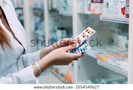 Pharmacist holding medicine box and capsule packs in pharmacy drugstore Royalty-Free Stock Photo #2054540627
