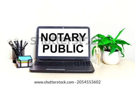 On the desktop is a potted plant, stationery and an open laptop with the text NOTARY PUBLIC on the screen. Home Office.
