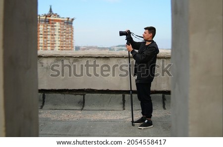 Young white Caucasian man taking cityscape photo on building rooftop on sunny day         