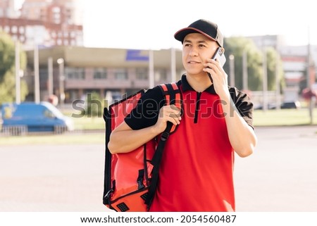 Food delivery guy with red backpack deliver orders. Male courier with isothermal food case box arrives to the entrance to the house and calls for client