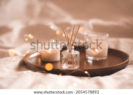 Home perfume in glass bottle with wood sticks, scented burn candles  tray in bedroom close up. Aromatherapy cozy atmosphere lifestyle. Winter warm xmas season.  Royalty-Free Stock Photo #2054578892