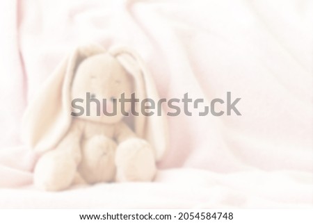 Children's background with a bunny toy. A soft, stuffed rabbit on a pink blanket. Toy in the children's room. Transparent blurred background.