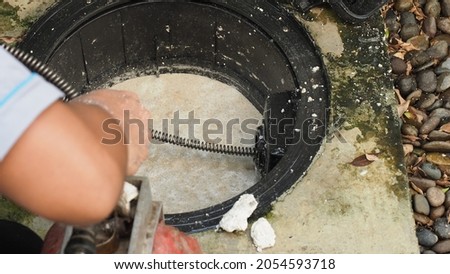 Drain cleaning. Plumber repairing clogged grease trap with auger machine. Maintenance the sewage system and grease trap by professional plumber. Using auger snake to fix and unclog a drain. Royalty-Free Stock Photo #2054593718
