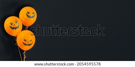 Orange balloons with no glare isolated on textured black background for Happy Halloween celebration. Halloween banner with helium balloons with scary pumpkin faces with copy space.