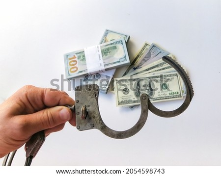 Shot of a hand holding police handcuffs on top of bundles of paper money. Twenty thousand American dollars. The concept of fighting corruption.                      