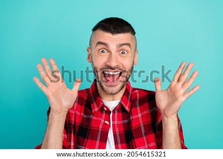 Photo of impressed millennial brunet guy hands up wear checkered shirt isolated on teal color background