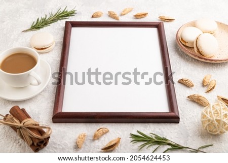 Brown wooden frame mockup with cup of coffee, almonds and macaroons on gray concrete background. Blank, side view, still life.
